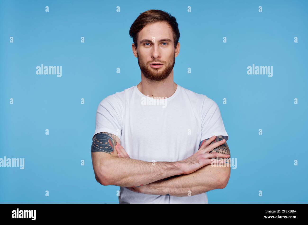 beau homme en t-shirt blanc tatouages sur ses bras court afficher l'arrière-plan bleu Banque D'Images