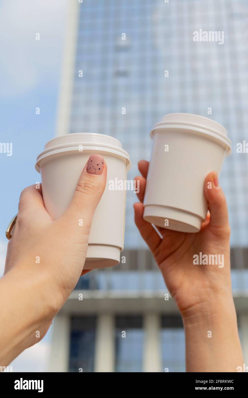 Deux tasses blanches avec café pour aller dans les mains des femmes sur fond de bâtiments de la ville et du ciel Banque D'Images
