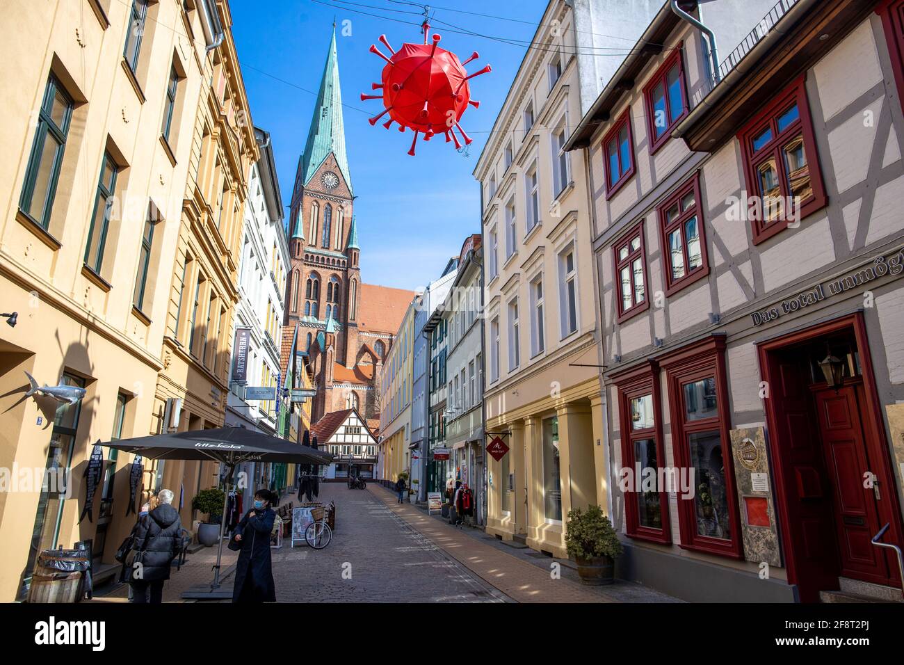 Schwerin, Allemagne. 15 avril 2021. Un coronavirus fait maison surplombe une rue commerçante en face de la tour de la cathédrale de Schwerin. Un poissonnier vivant dans la rue a construit la lanterne à l'image du virus et l'a accrochée. Compte tenu de l'augmentation rapide des taux d'infection de la couronne, le gouvernement de l'État de Mecklembourg-Poméranie occidentale consulte les représentants des autorités locales, de l'industrie et des associations sur des mesures plus sévères pour lutter contre la pandémie. La conférence en ligne a été avancée un jour en raison du développement dynamique. Credit: Jens Büttner/dpa-Zentralbild/dpa/Alay Live News Banque D'Images