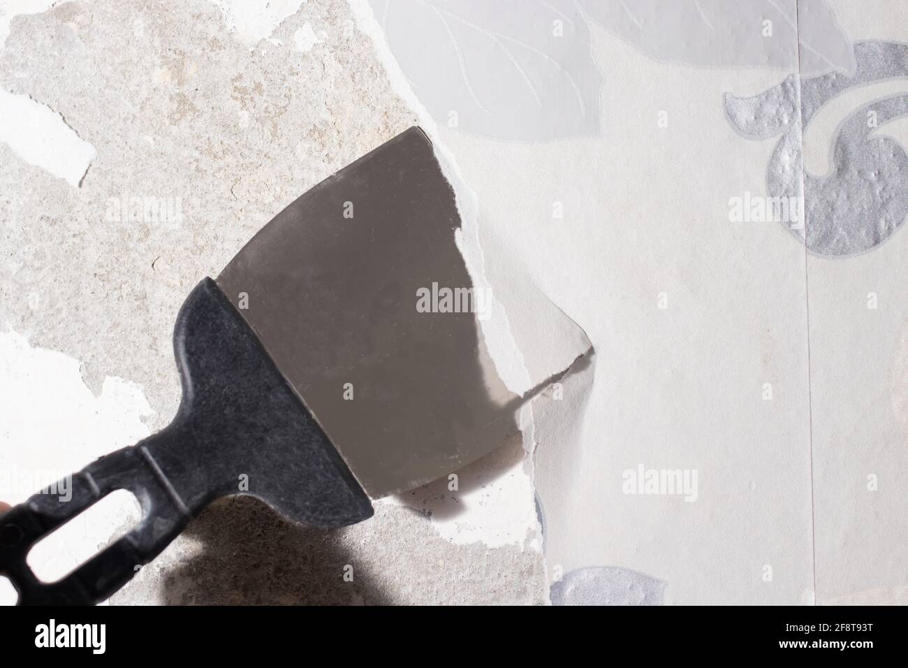 Le réparateur retire le papier peint bancal usagé du mur à l'aide d'une spatule. Élimination des résidus de papier peint pendant les réparations. Banque D'Images