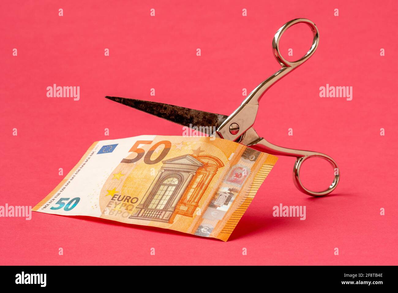 Couper cinquante euros avec des ciseaux sur fond rose. Concept sur le thème de la dévaluation de l'argent. Banque D'Images