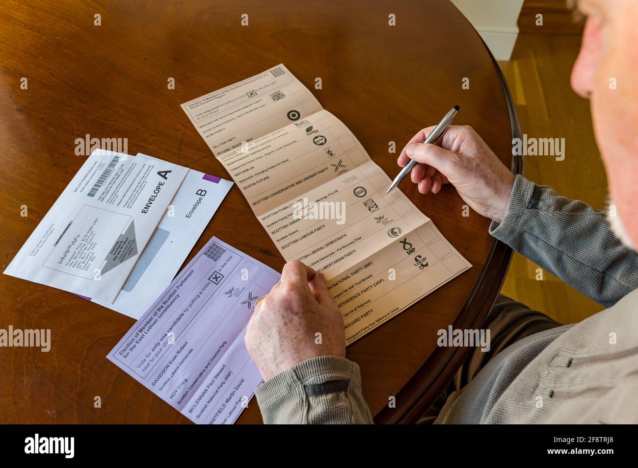 East Lothian, Écosse, Royaume-Uni, 15 avril 2021. Les bulletins postaux arrivent pour les élections écossaises : les résidents du comté peuvent voter pour la MSP du Lothian est et la région du sud de l'Écosse. Les candidats pour les premiers sont Euan Davidson (Démocrates libéraux écossais), Craig Hoy (conservateurs écossais et unionistes), Paul McLennan (SNP) et Martin Whitfield (Parti travailliste écossais et ancien député qui a perdu en 2019 à Kenny MacAskill, qui est en lice pour Alba). La liste régionale comprend 16 parties. Un homme considère pour qui voter sur le bulletin de vote Banque D'Images