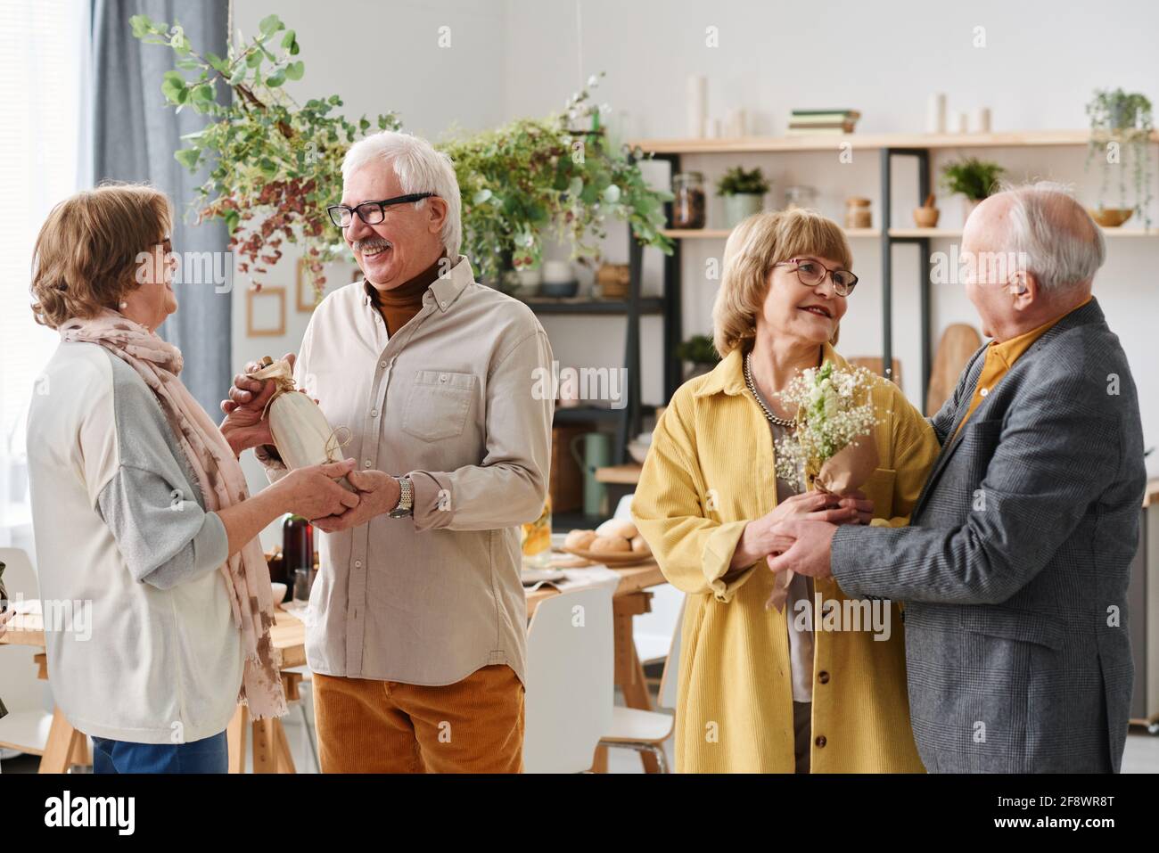 Un groupe d'amis seniors se rencontrent les uns avec les autres présente et parle en se tenant debout dans la pièce Banque D'Images