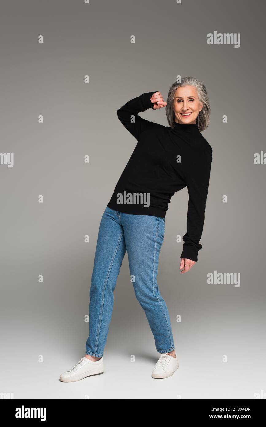 Femme joyeuse aux cheveux gris posant sur fond gris Banque D'Images