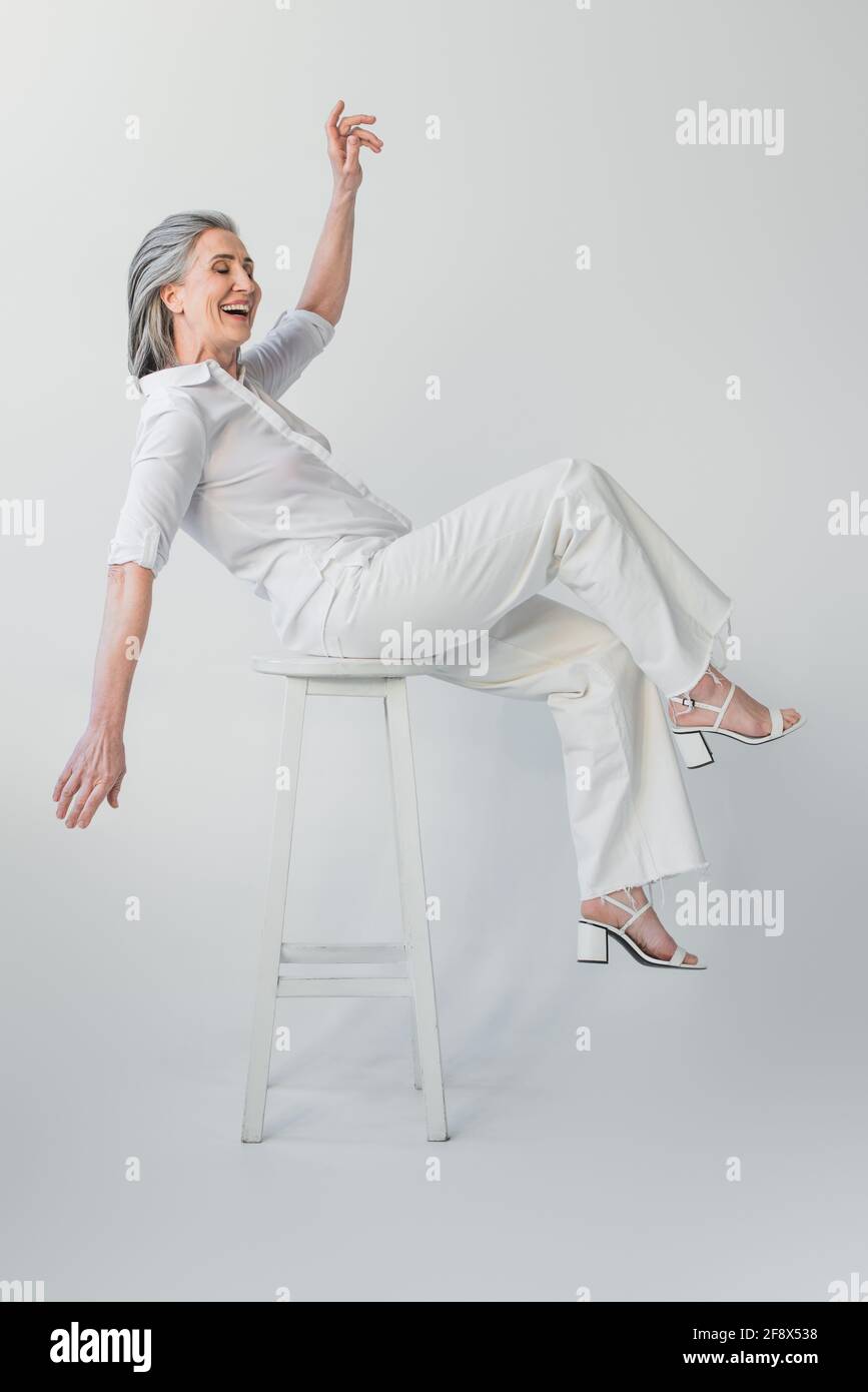 Femme mûre positive souriant sur chaise sur fond gris Banque D'Images