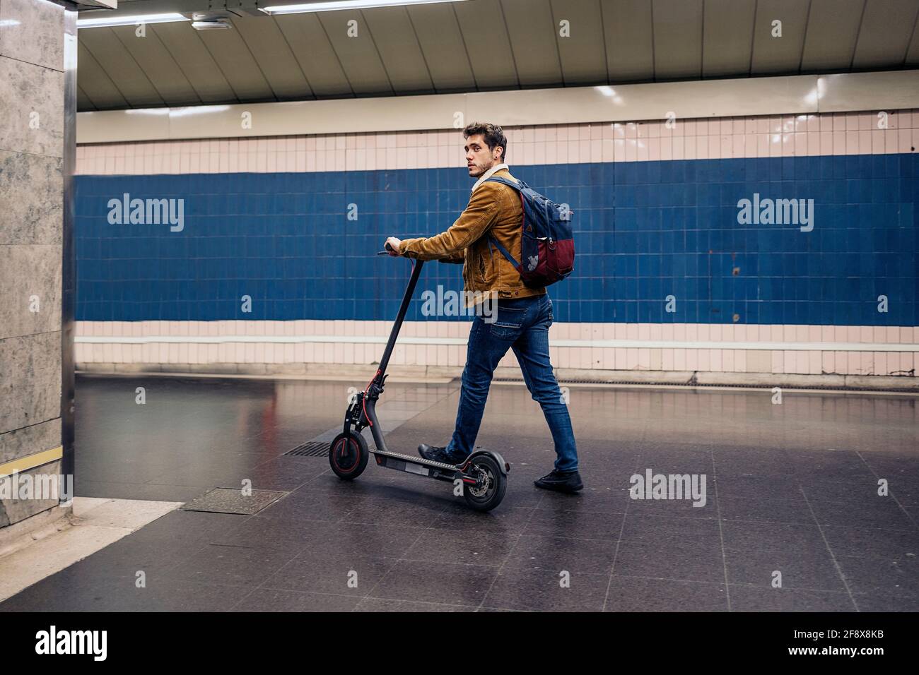 Homme dans une tenue élégante marchant avec un scooter électrique dans le souterrain Banque D'Images