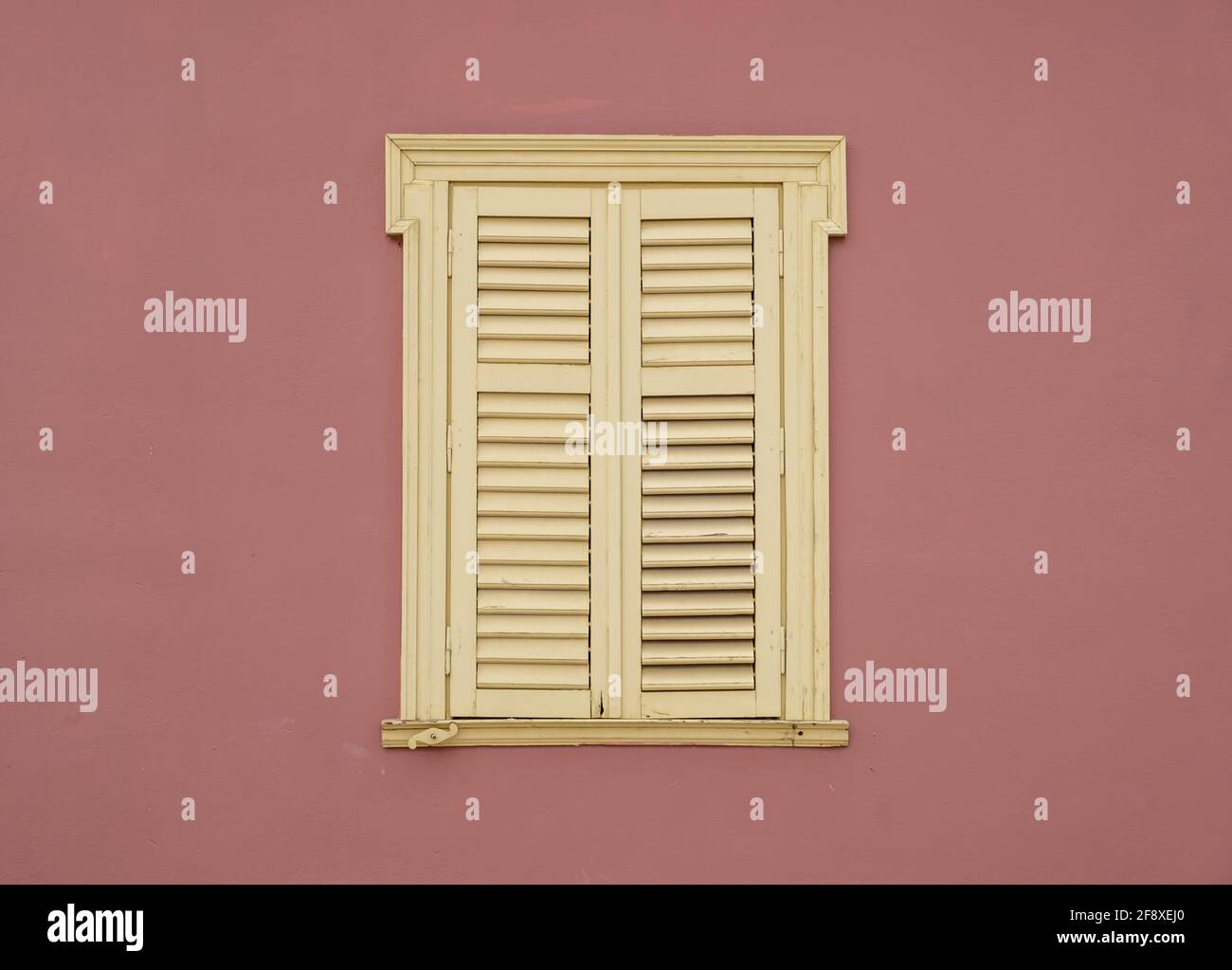 Fenêtre volets en bois sur fond de mur peint de couleur marron. Stores à fenêtre fermée de style français pâle jaune avec cadre ornemental sur un buil résidentiel Banque D'Images