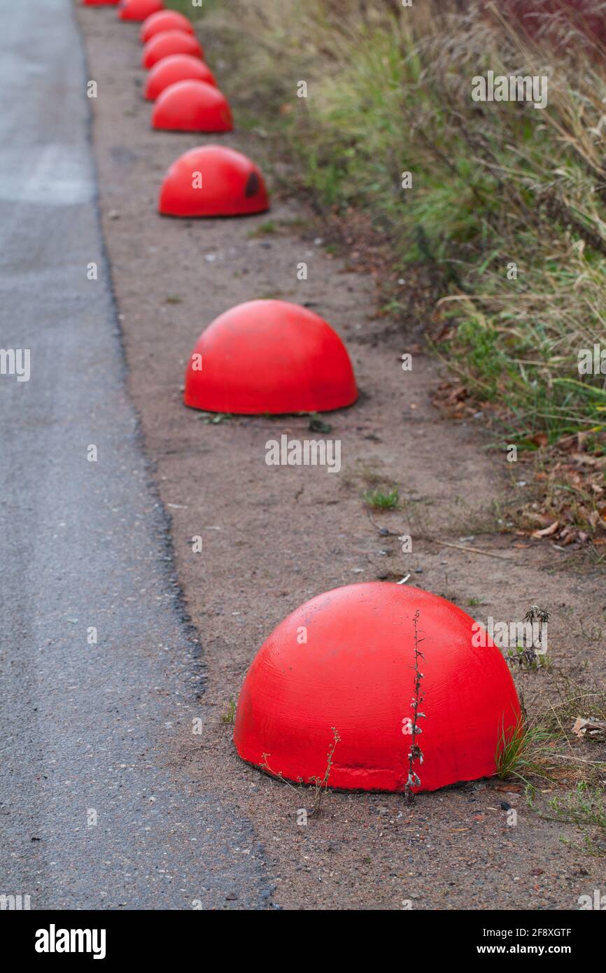 Des bollards en béton rouge anti-stationnement en forme d'hémisphère se tiennent dans une rangée le long un bord de route Banque D'Images