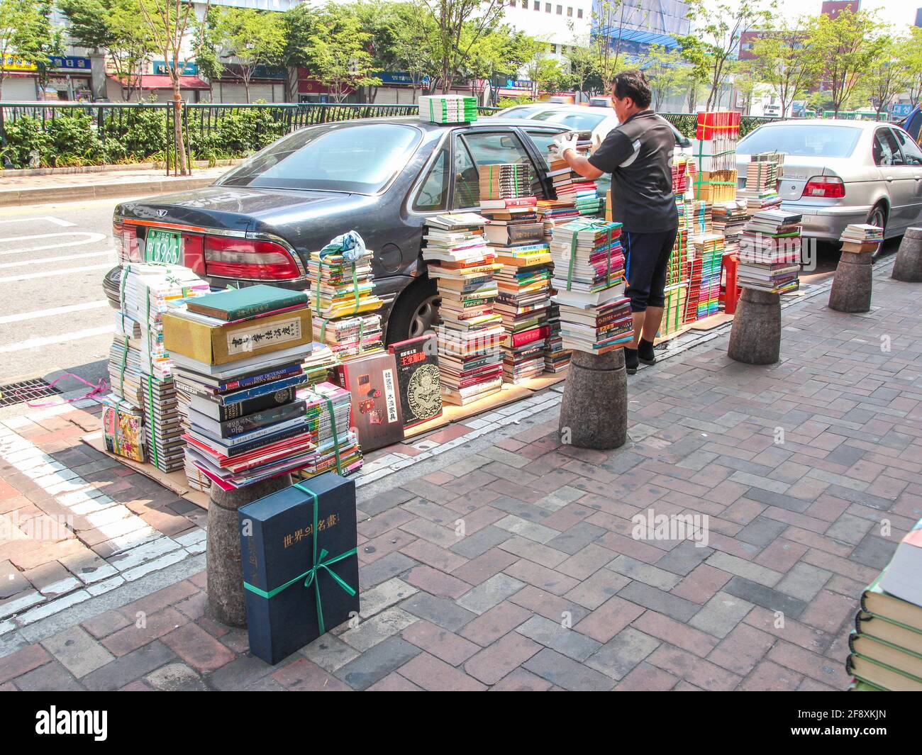 Un fournisseur empile les livres sur un trottoir autour d'une voiture garée, en les préparant à vendre. À Séoul, en Corée du Sud. Banque D'Images