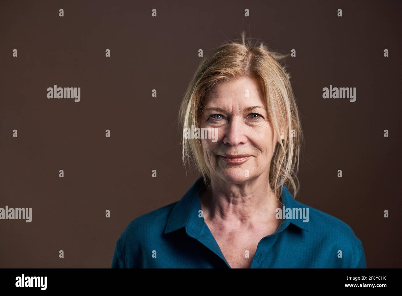 Gros plan d'une femme âgée aux cheveux blonds et en chemisier regarder la caméra isolée sur fond noir Banque D'Images