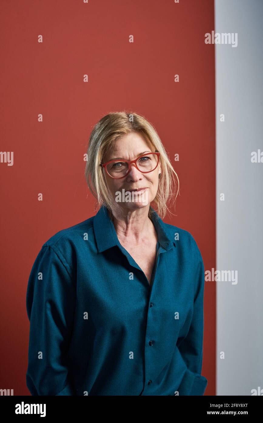 Portrait d'une femme d'affaires élégante et âgée en chemisier et lunettes à la caméra isolée sur fond rouge Banque D'Images