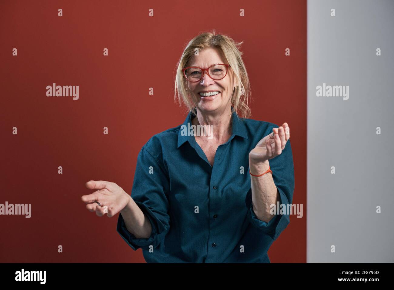 Portrait d'une femme âgée heureuse en blouse bleue debout et riant sur fond rouge Banque D'Images