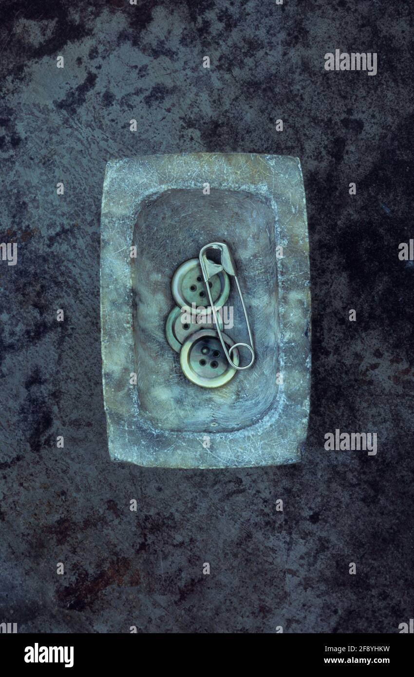 Goupille de sécurité argentée dans un petit plat en marbre gris avec trois boutons en nacre Banque D'Images