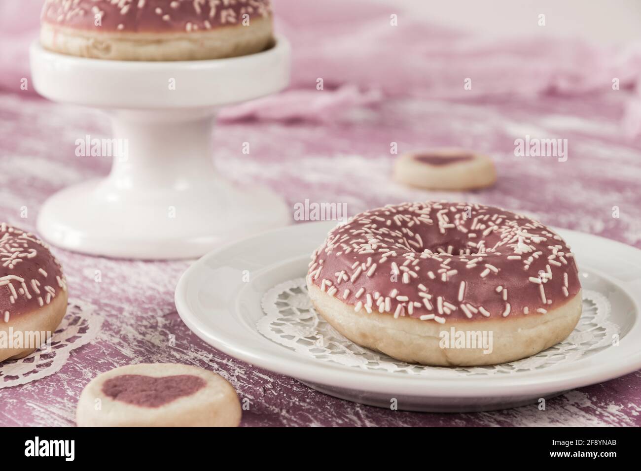 Beignets vernis roses avec biscuits en forme de coeur sur fond peint rose et blanc, couleurs désaturées pour un look vintage monochrome Banque D'Images