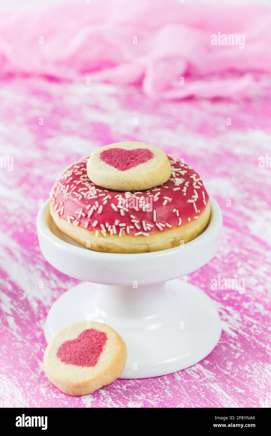 Beignet rose avec biscuits de coeur sur fond peint rose et blanc, vertical avec espace de copie Banque D'Images