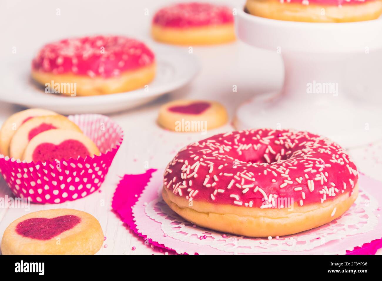 Beignet verni rose sur blanc, décoré de biscuits et d'autres beignets en arrière-plan Banque D'Images