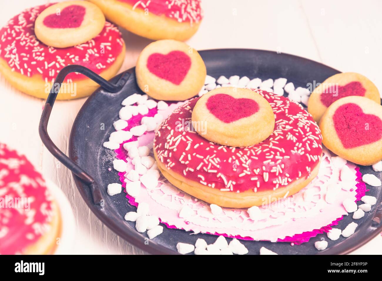 Beignet glacé rose et biscuits avec coeurs sur un métal plateau sur une table blanche Banque D'Images