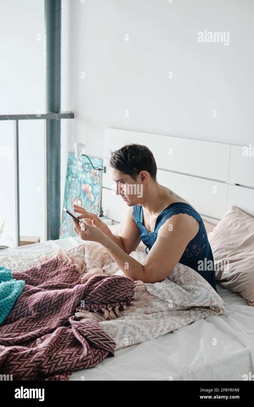 Transgenre en pyjama femme envoyant un message sur son mobile téléphone  tout en étant assis dans le lit le matin Photo Stock - Alamy
