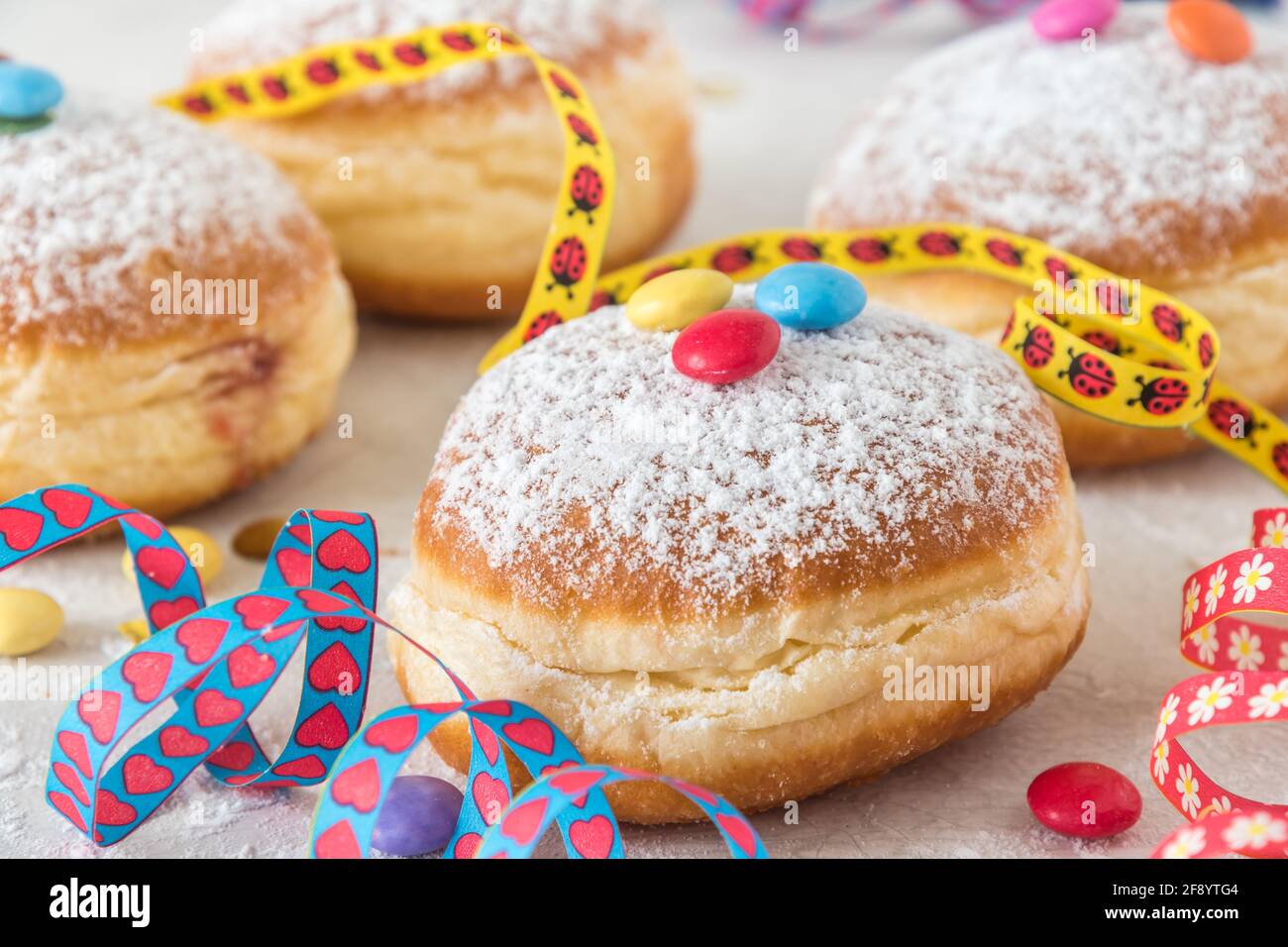 Krapfen, Berliner ou donut avec des banderoles, des confetti et des grains de chocolat sur fond blanc. Image de carnaval ou d'anniversaire colorée. Banque D'Images