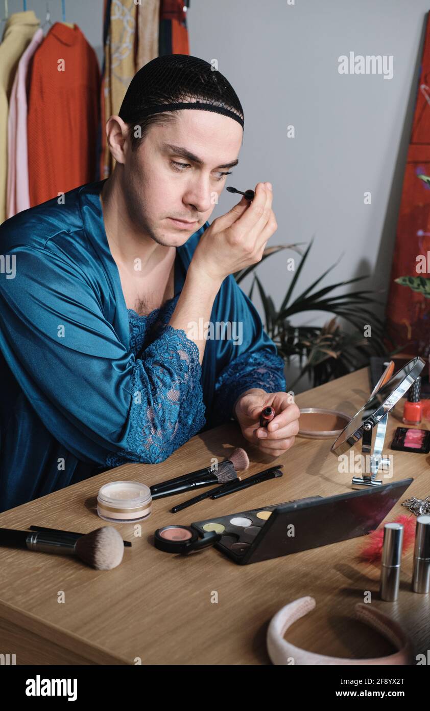 Jeune homme transgenre appliquant le maquillage à la table qu'il applique mascara sur les yeux Banque D'Images