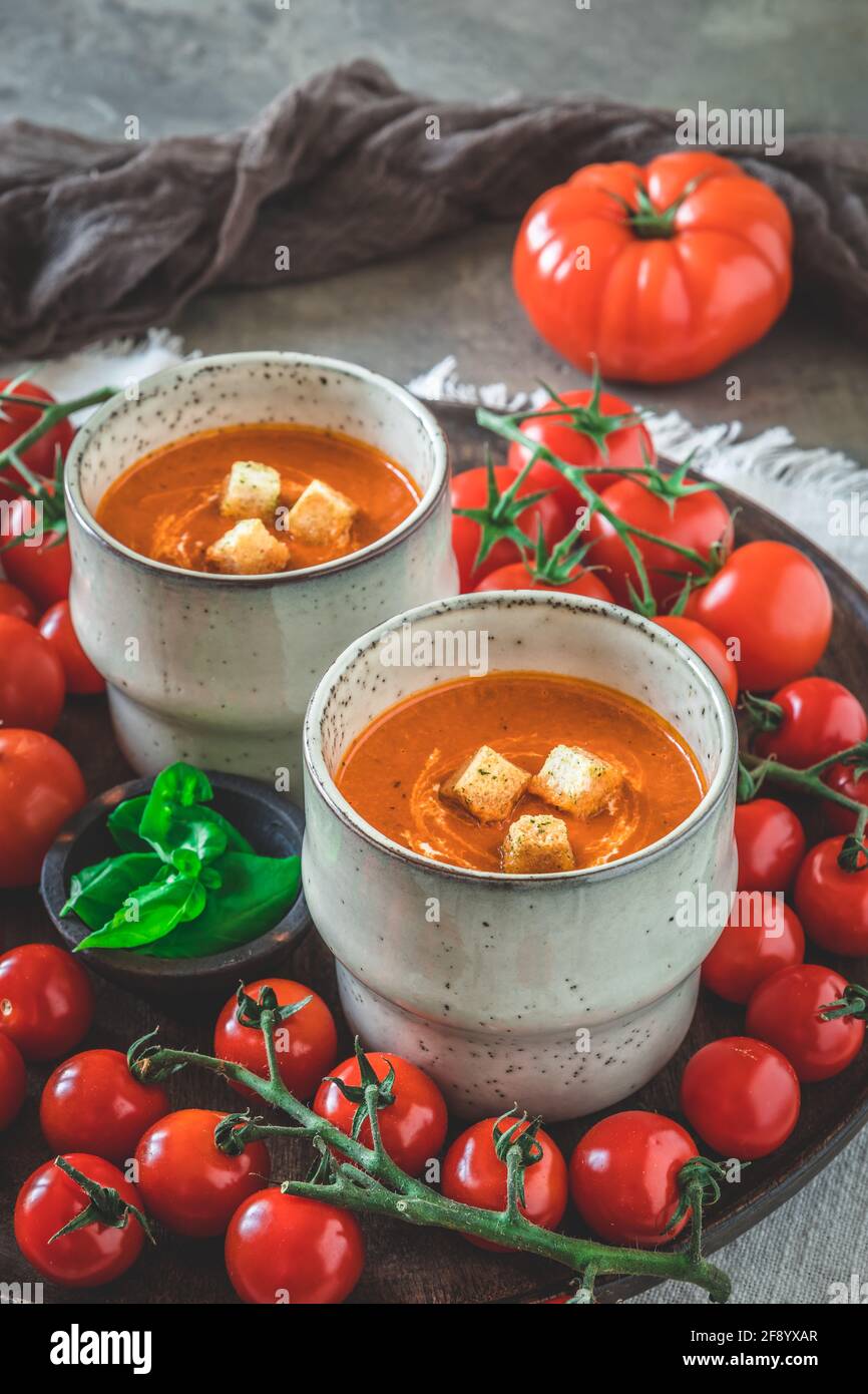 Deux tasses remplies de soupe de tomates maison sur une assiette en bois avec une variété de tomates mûres, verticales Banque D'Images