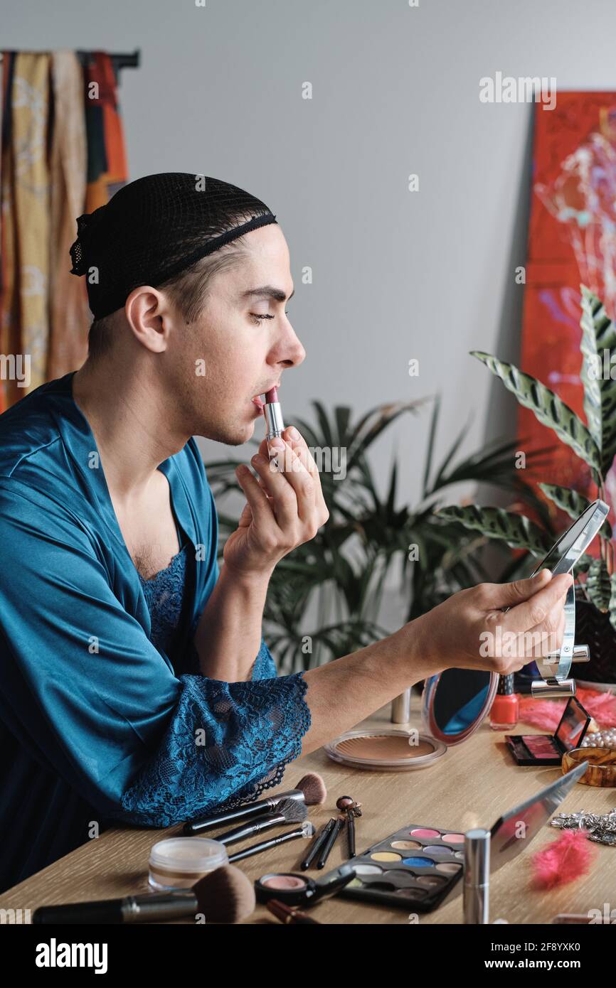 Jeune homme transgenre appliquant le rouge à lèvres tout en regardant le miroir à accueil Banque D'Images