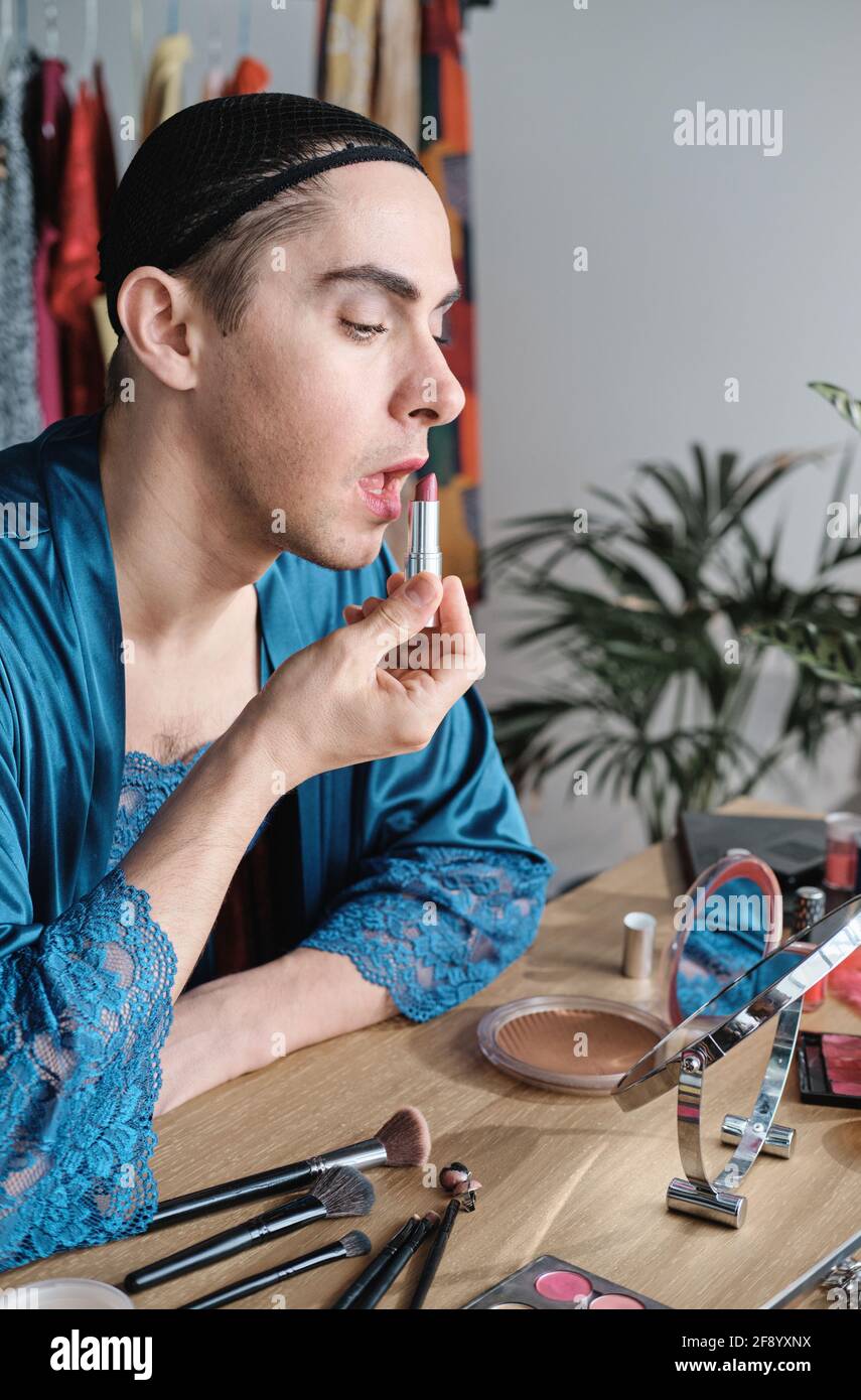 Jeune homme féminin assis à la table et appliquant du rouge rouge à lèvres sur ses lèvres Banque D'Images