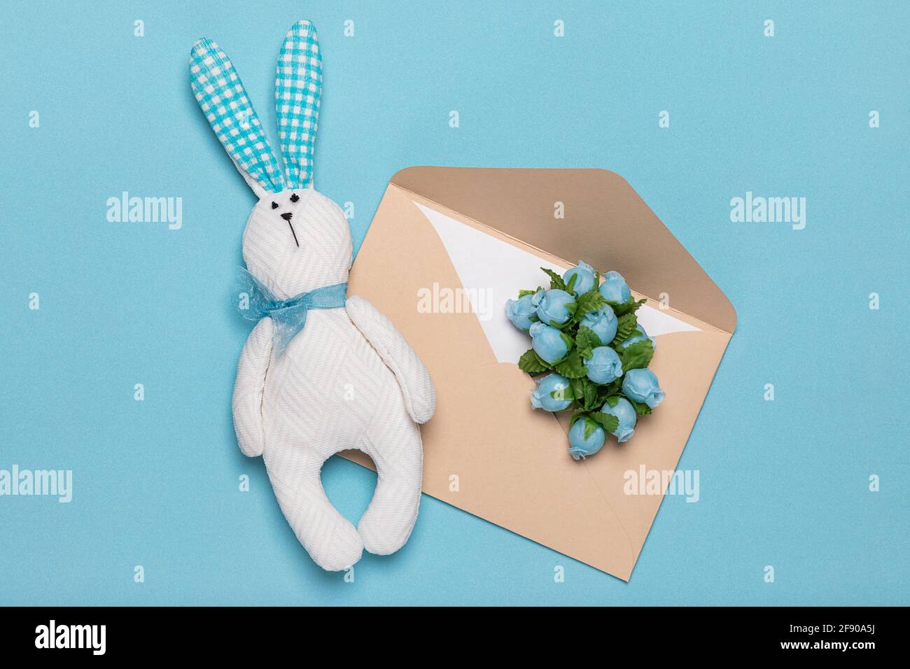 Jouet blanc lapin lièvre fait à la main et enveloppe en papier avec des fleurs délicates plat sur fond bleu. Concept de printemps et romance de lettres et de carte Banque D'Images