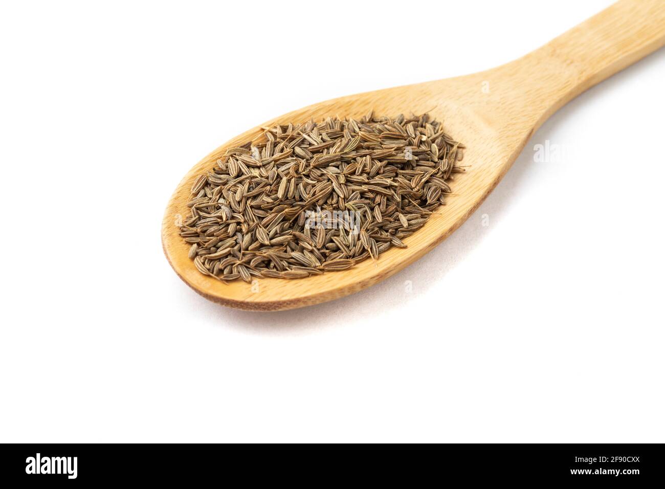 Gros plan des graines de cumin sur une cuillère en bois isolée sur fond blanc. Banque D'Images