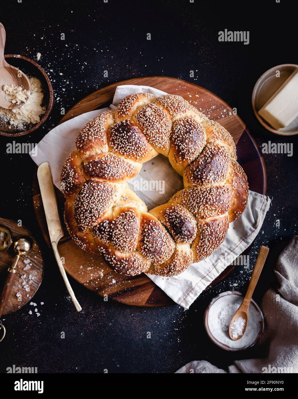 Une couronne de pain au sésame Challah est placarde sur une planche ronde en bois, avec de la farine, de l'assaisonnement et du beurre Banque D'Images