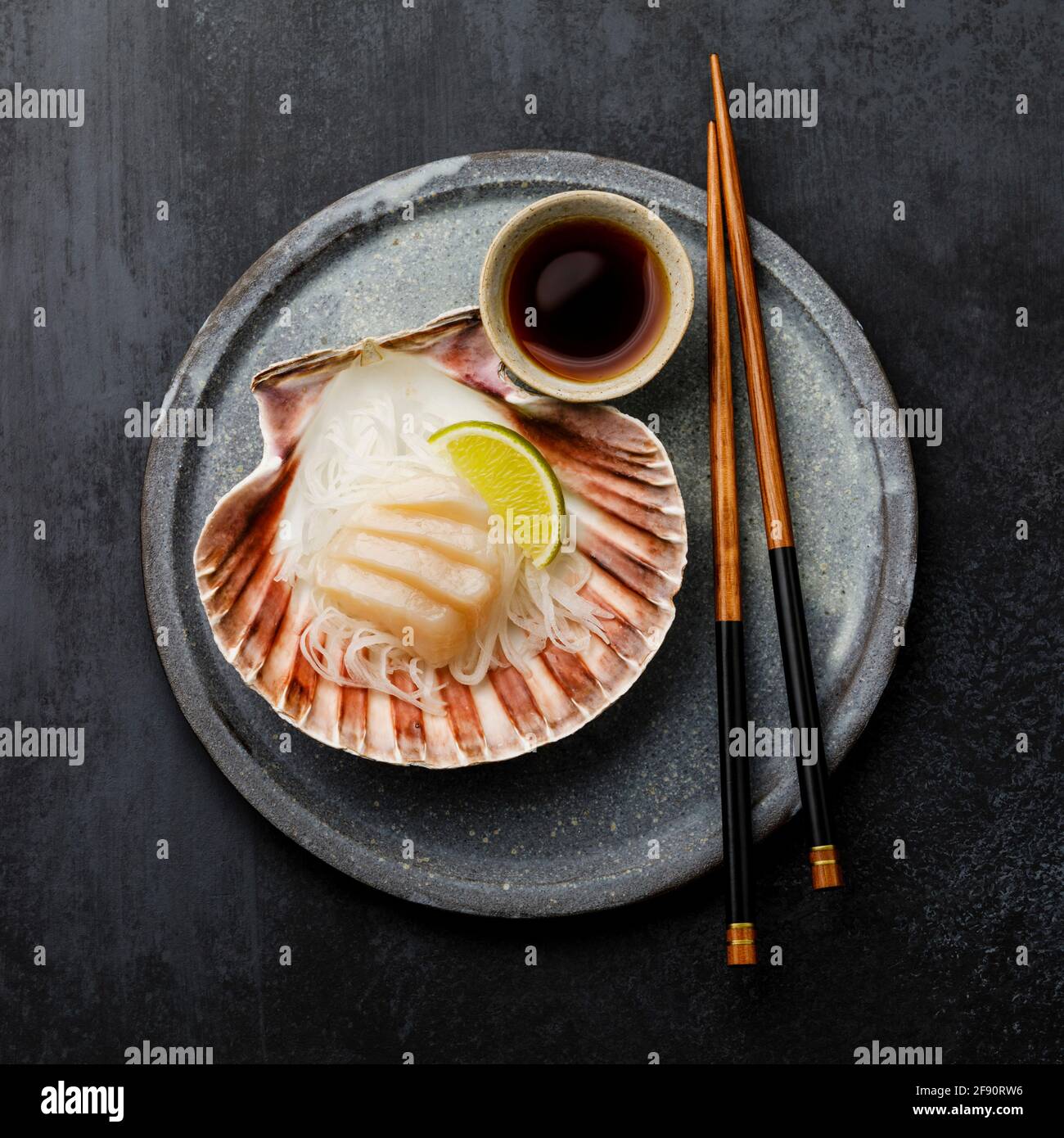 Sashimi de pétoncles vivants en carapace avec du daïkon, de la lime et de la sauce soja sur fond sombre Banque D'Images