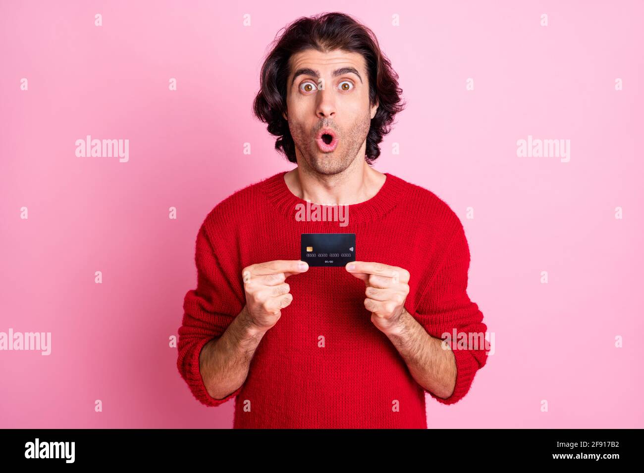 Photo portrait de l'homme choqué tenant la carte de crédit en deux mains isolées sur fond rose pastel Banque D'Images