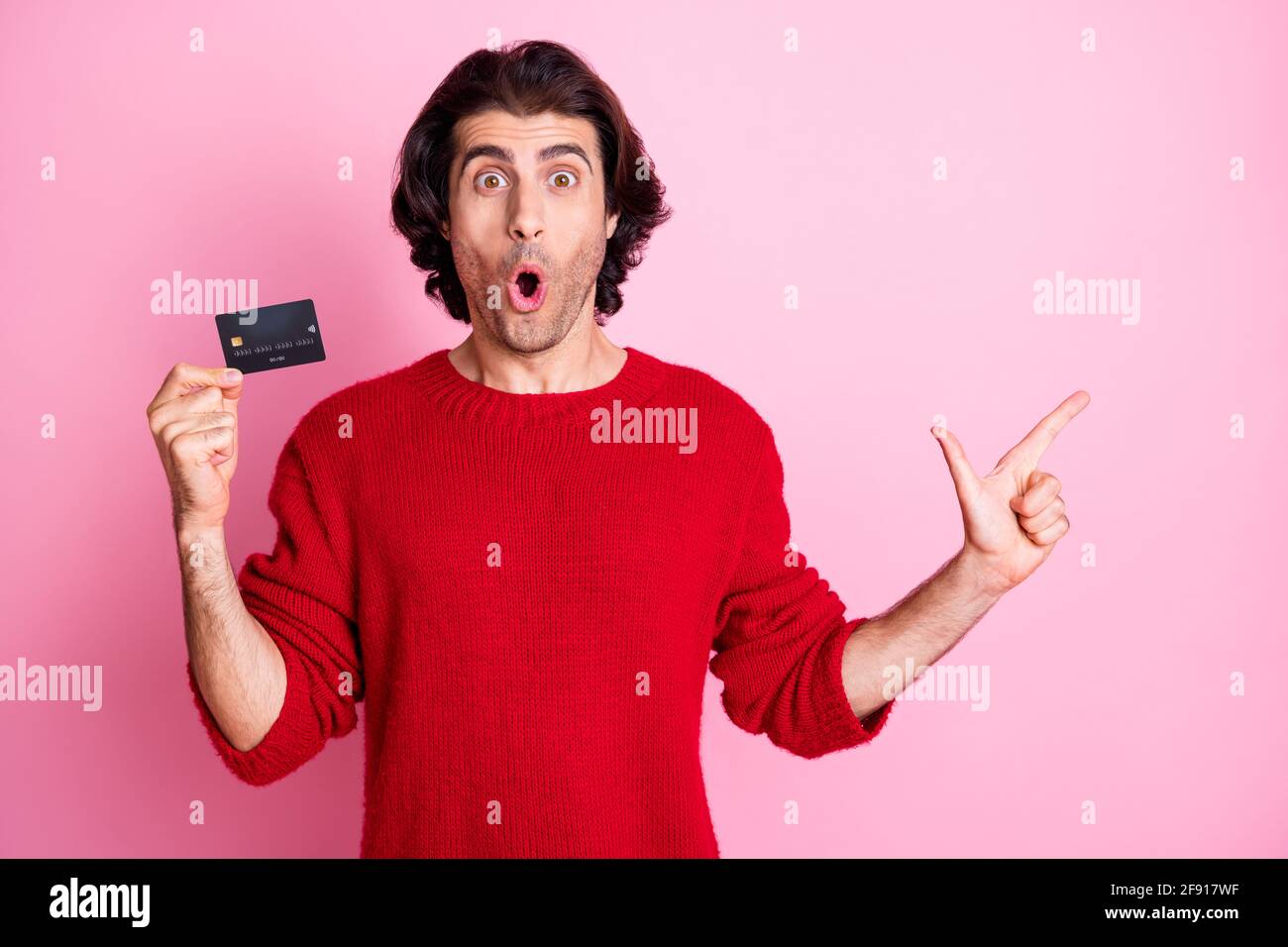 Photo portrait d'un homme choqué pointant du doigt vers un espace vide tenir la carte de crédit dans une main isolée sur rose pastel arrière-plan coloré Banque D'Images