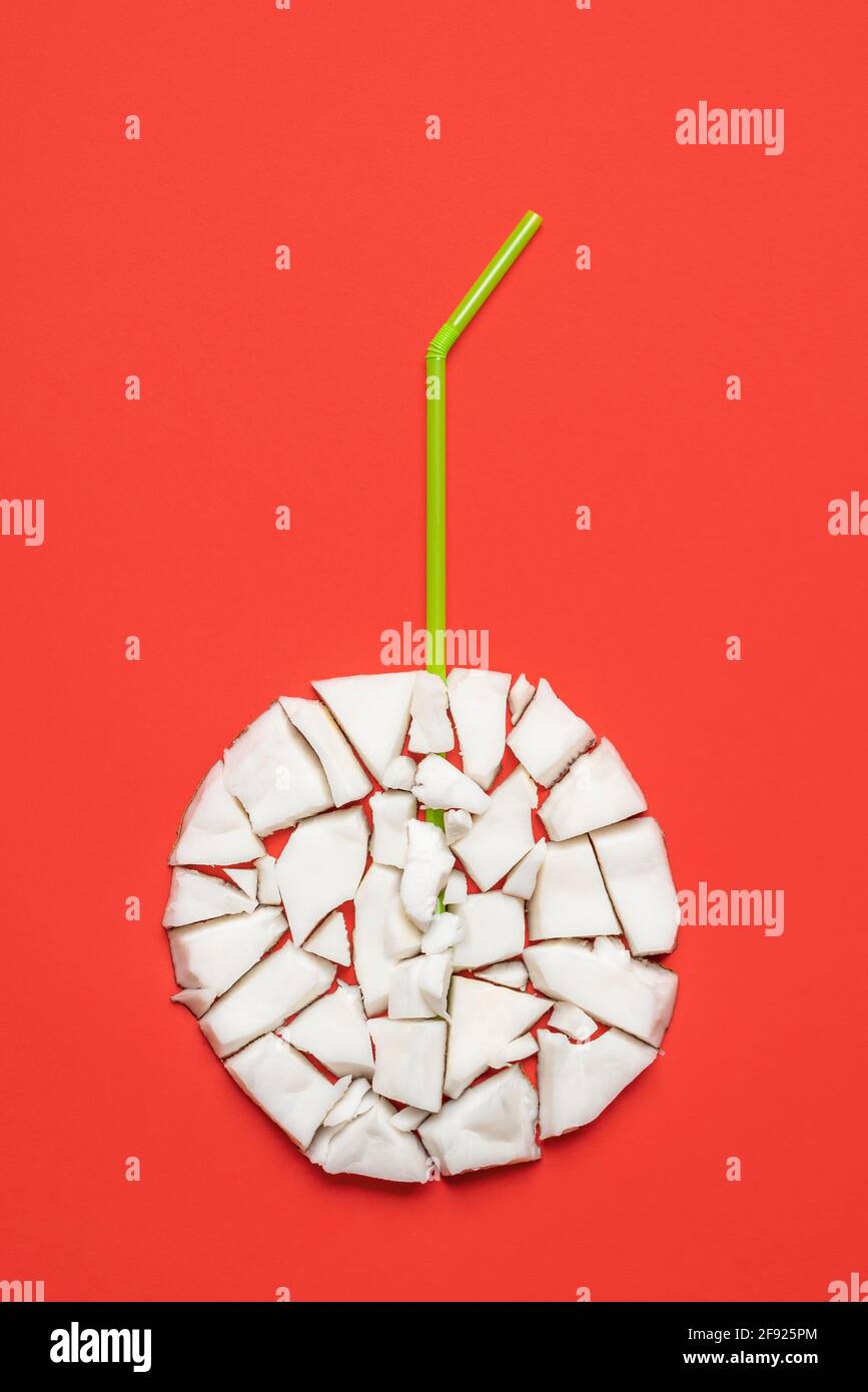 Concept de boisson d'été avec des pièces de noix de coco disposées dans un cercle et une paille à boire, isolée sur fond rouge. Banque D'Images