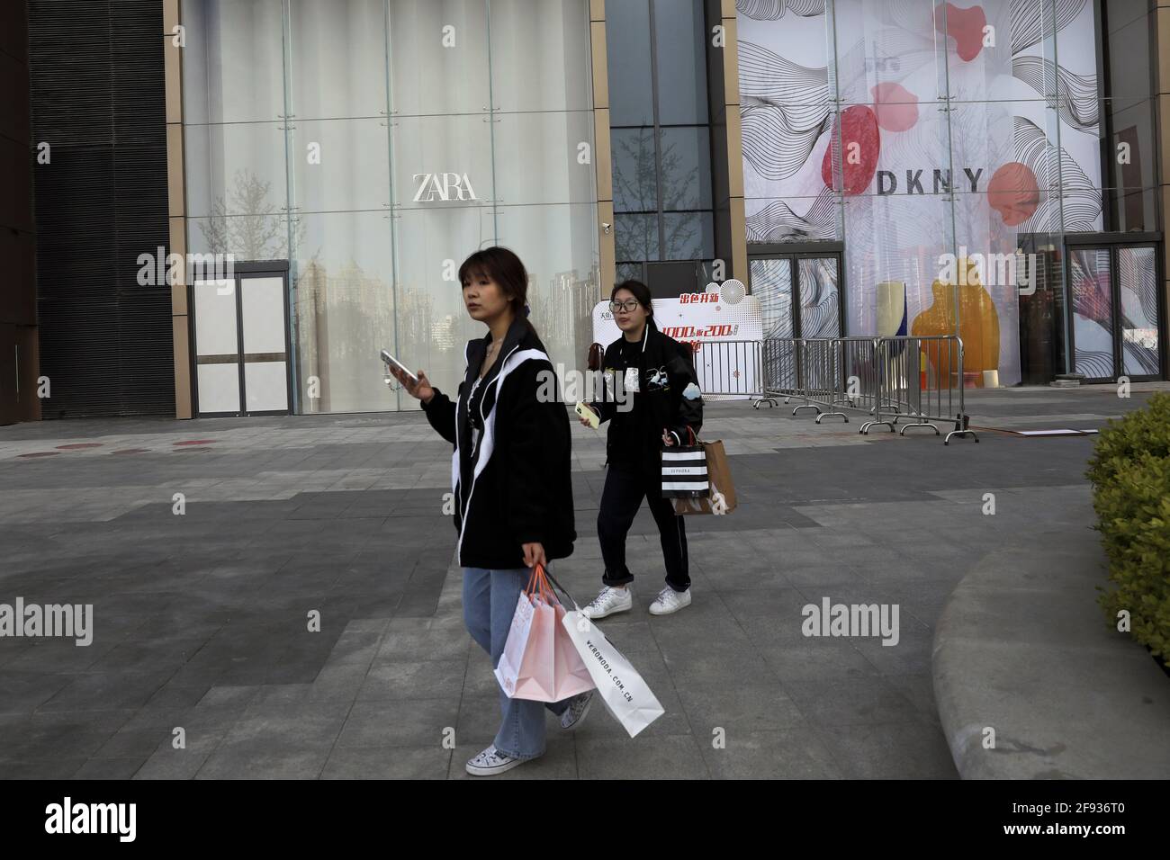 Les clients se promène devant les magasins de vêtements de DKNY et de la  marque Zara d'Inditex dans un centre commercial récemment ouvert à Beijing,  en Chine, le 16 avril 2021. REUTERS/Tingshu