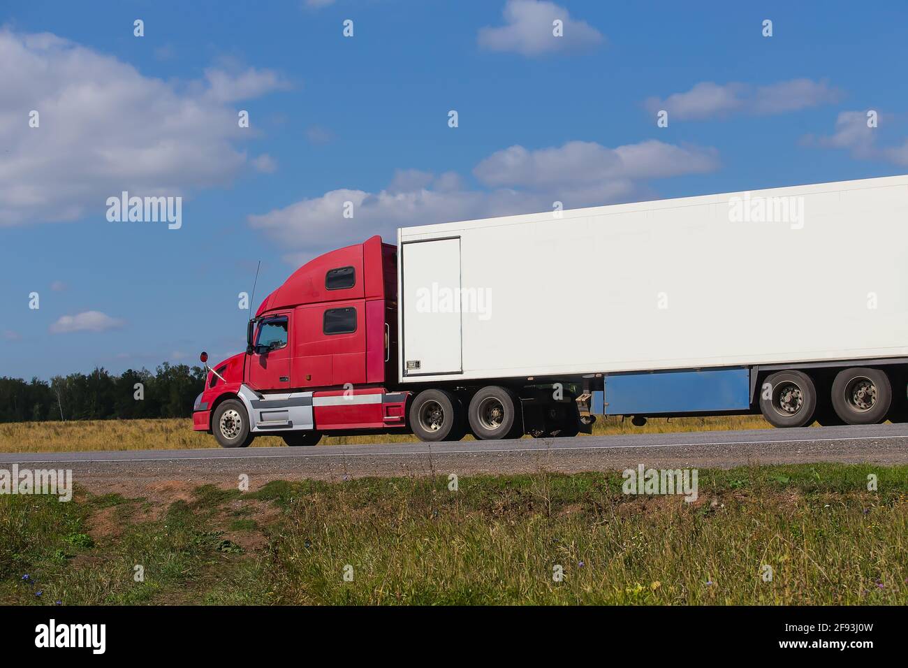 Une grande semi-remorque se déplace sur une route de campagne par une journée d'été. Banque D'Images
