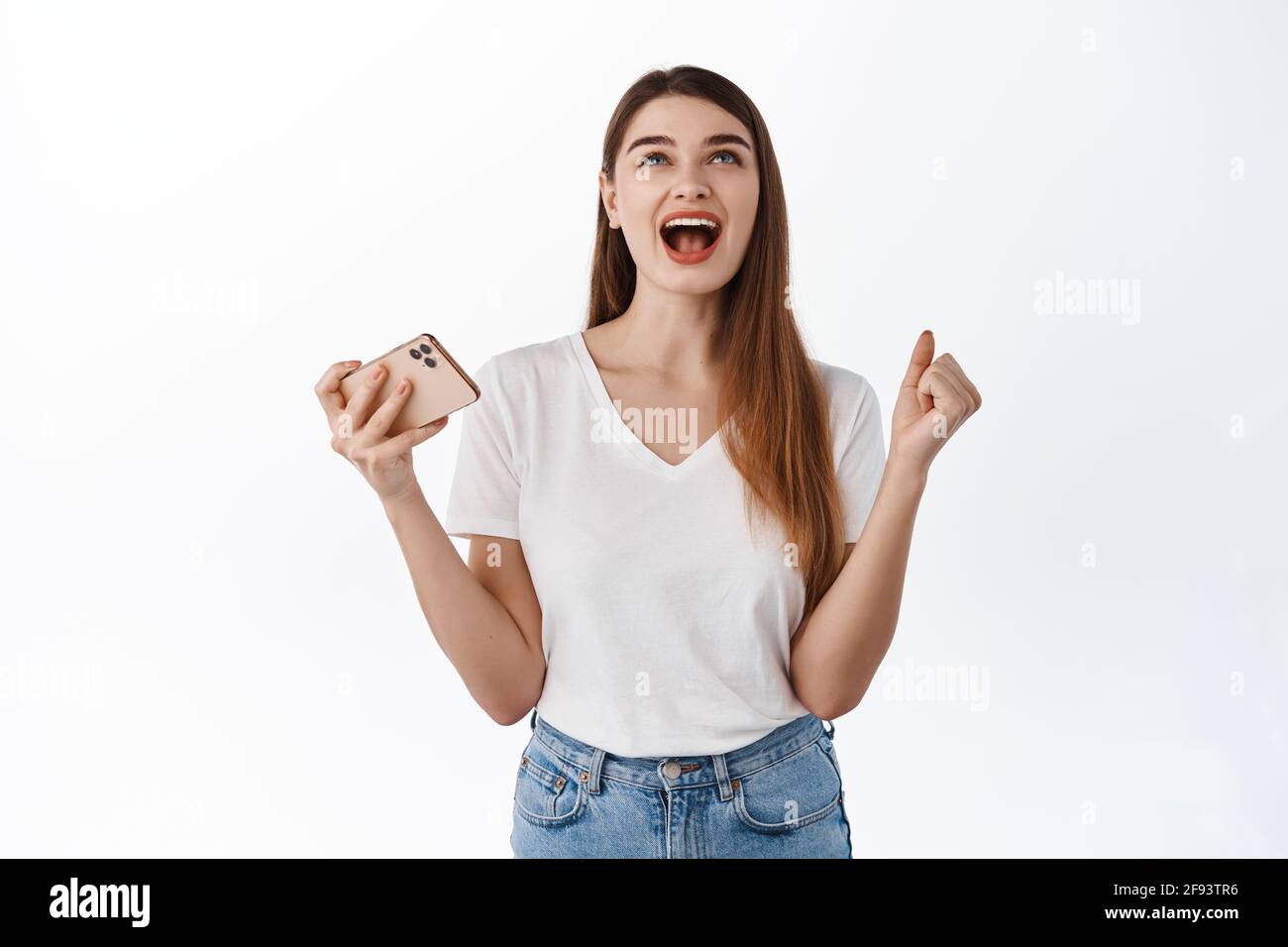 Femme soulagée et heureuse criant oui et recherchant satisfaite, tenant le smartphone, gagnant en ligne sur le téléphone mobile, atteindre l'objectif d'application, gagner des résultats Banque D'Images