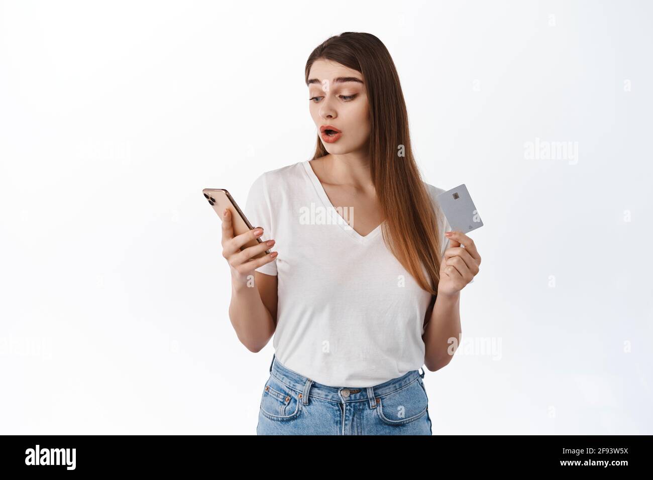 Femme semble surpris de son smartphone tout en payant avec la carte de crédit, les achats en ligne, l'assètement et la montée des sourcils intrigués avec quelque chose sur Banque D'Images