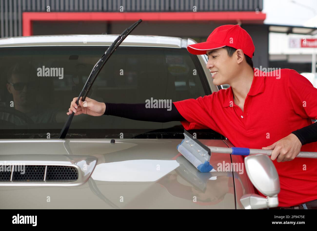 Un employé d'une station-service asiatique lève les essuie-glaces pour nettoyer le pare-brise de la voiture. Un conducteur caucasien avec des lunettes de soleil lève les pouces vers le haut pour exprimer son Banque D'Images