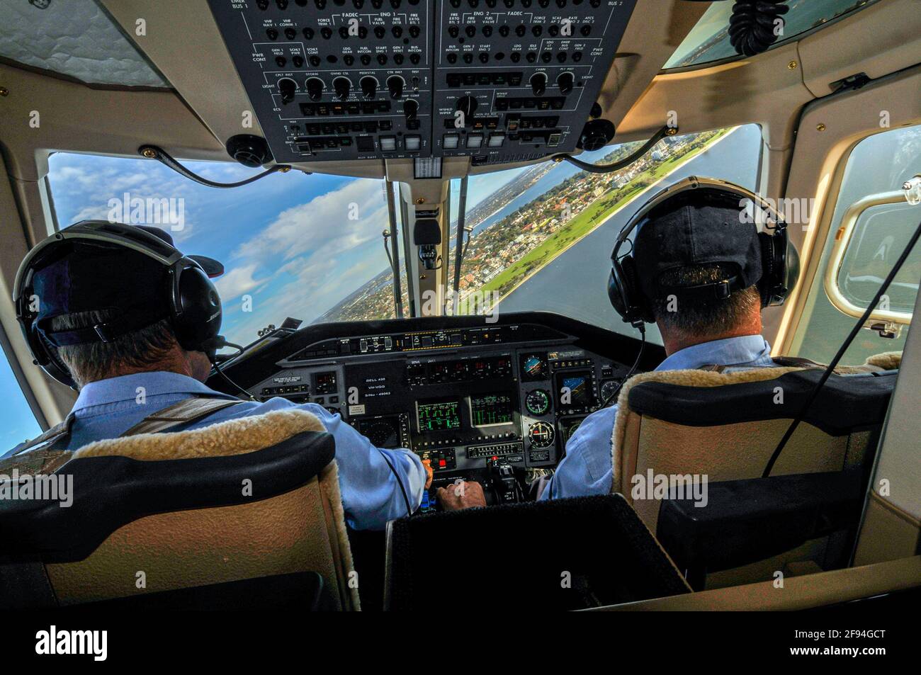 Vue de deux membres d'équipage à l'intérieur de la plate-forme d'un hélicoptère Bell 430 Dragonfly se trouvant au-dessus de la côte, avec une plage et un règlement urbain en vue. Banque D'Images