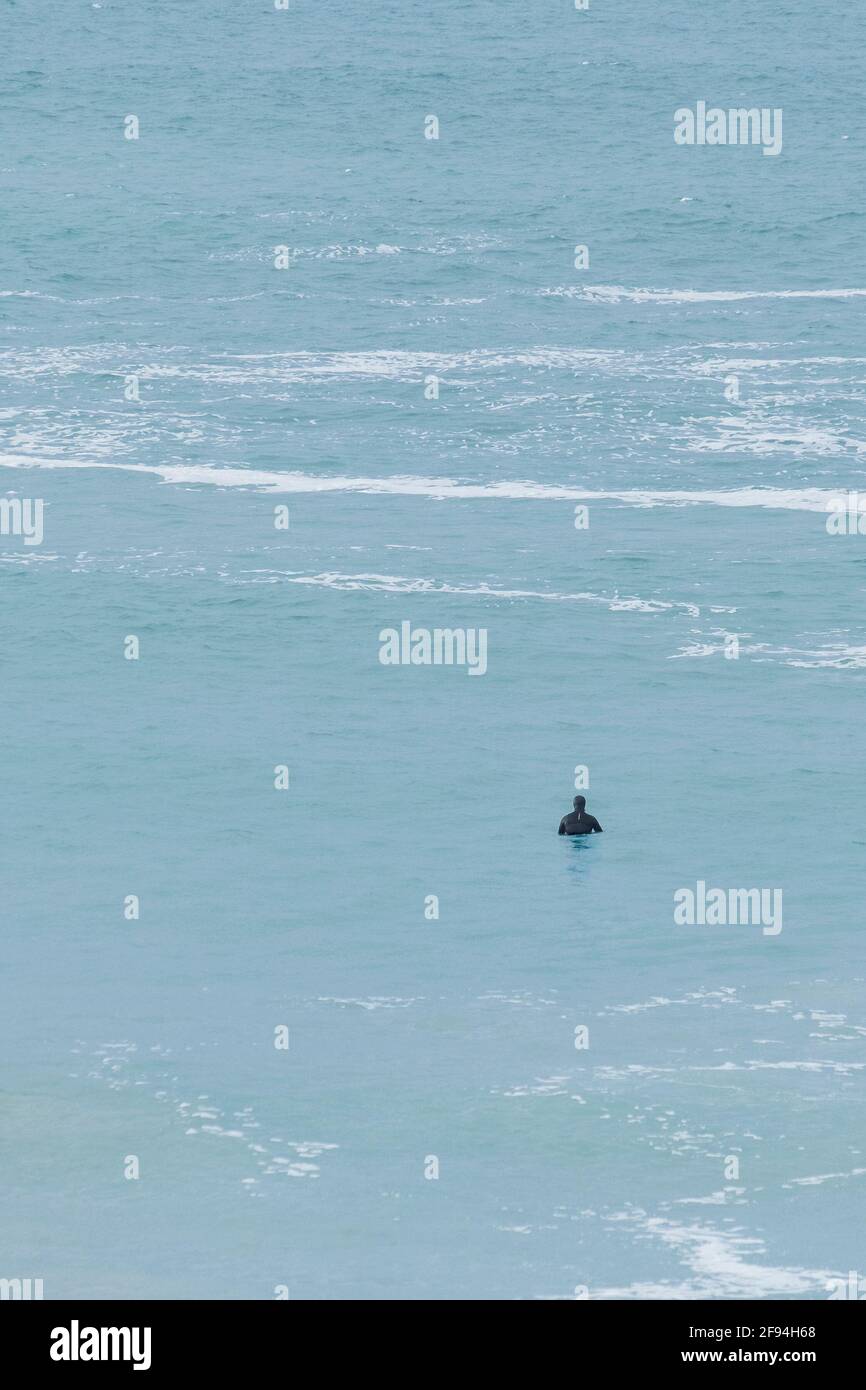 Un surfeur qui attend dans une mer calme pour une vague dans la baie de Fistral à Newquay, en Cornouailles. Banque D'Images