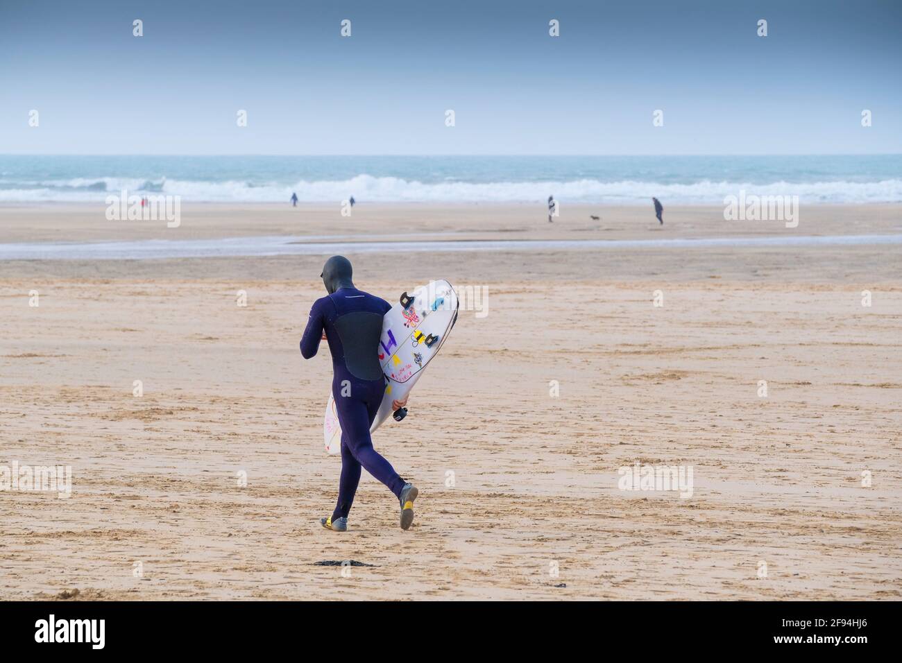 Un surfeur transportant sa planche de surf et traversant Crantock Beach à Newquay, dans les Cornouailles. Banque D'Images