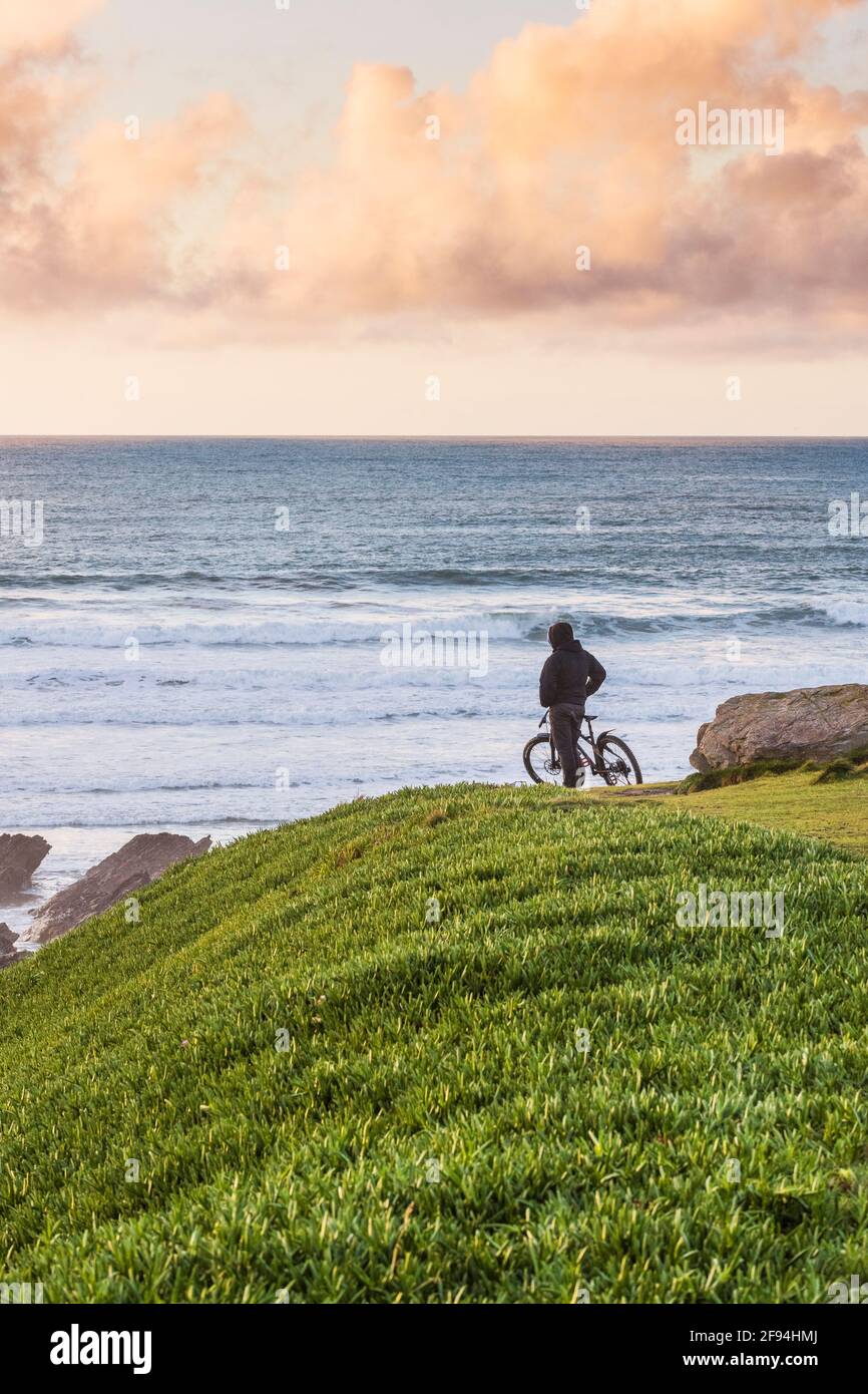 Un cycliste debout sur le promontoire qui regarde à la lumière du soleil en fin de soirée à Newquay, dans les Cornouailles. Banque D'Images