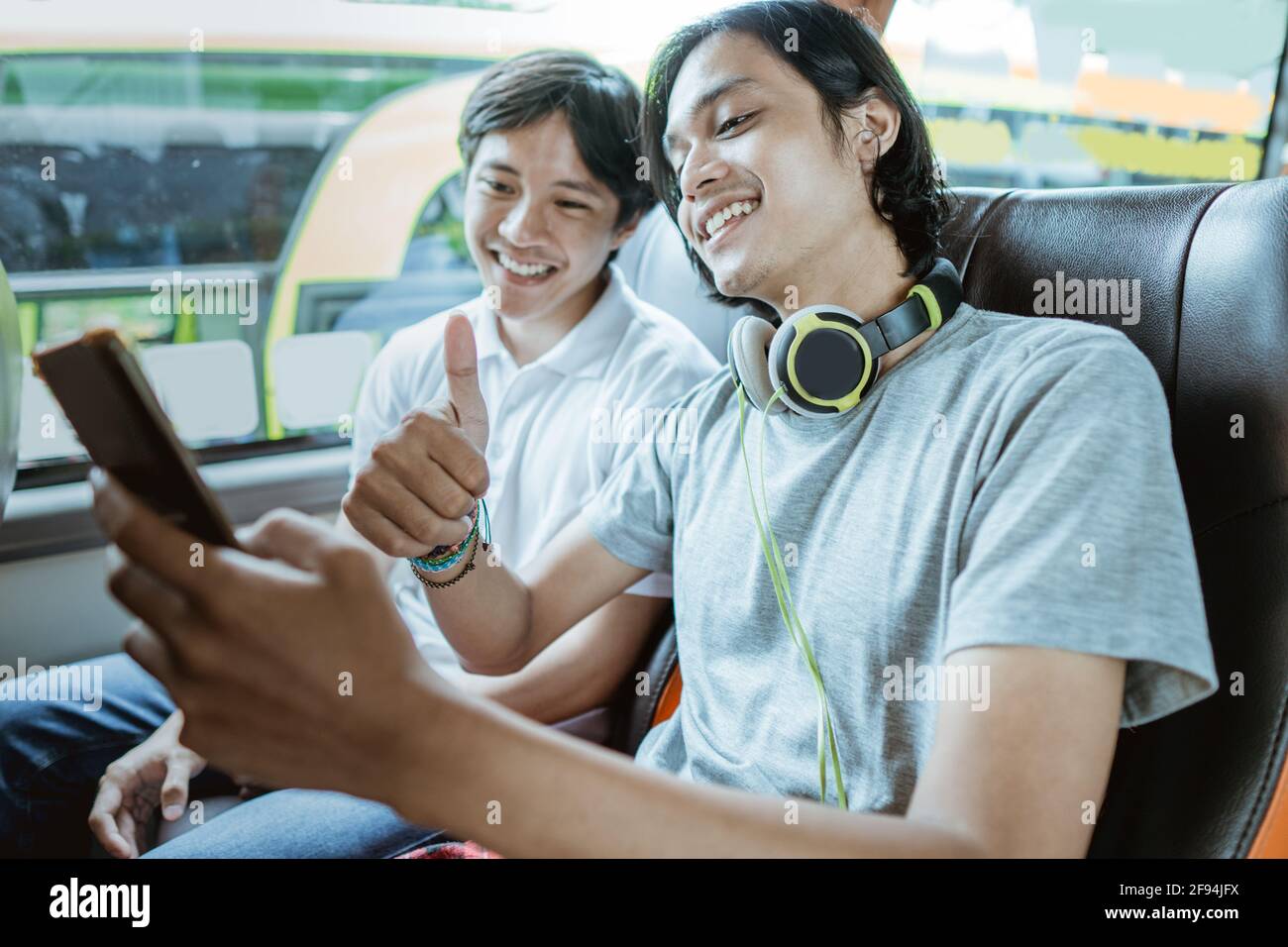 Un jeune homme asiatique avec un casque et utilisant un mobile téléphone pour les appels vidéo avec un pouce vers le haut Banque D'Images