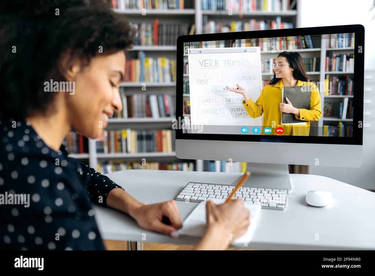 Vue sur l'épaule d'une étudiante afro-américaine intelligente sur un écran d'ordinateur avec une enseignante. Une enseignante conduit une leçon en ligne, une étudiante prend des notes. Formation en ligne, éducation Banque D'Images