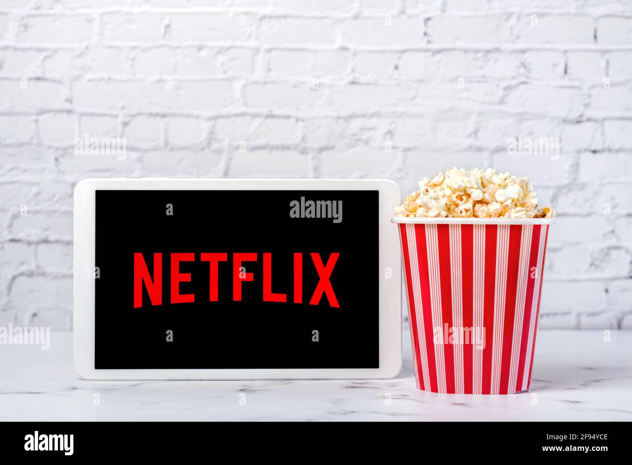 Logo Netflix sur l'écran d'une tablette numérique blanche avec pop-corn sur fond de briques blanches Banque D'Images