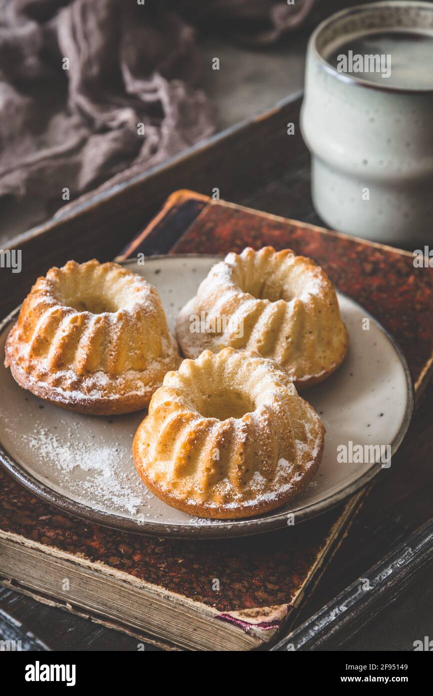 Trois petits gâteaux faits maison sur une assiette, une tasse de café et un vieux livre sur un plateau en bois sur fond gris, vertical Banque D'Images