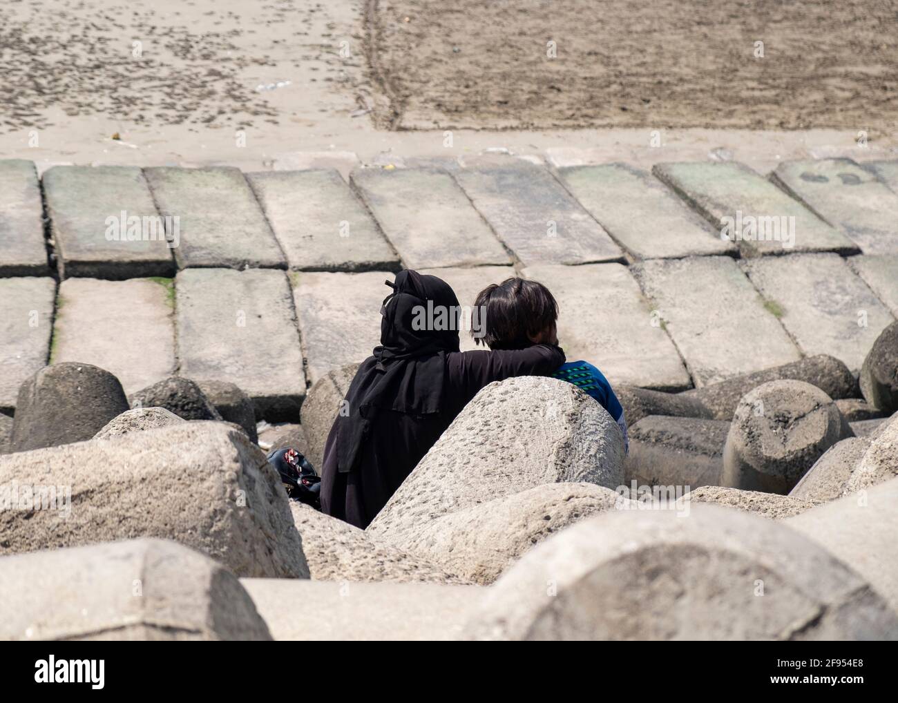 Jeune couple assis parmi des tétrapodes sur la plage de Mahim Bay à Mumbai, Maharashtra, Inde, Asie. Banque D'Images