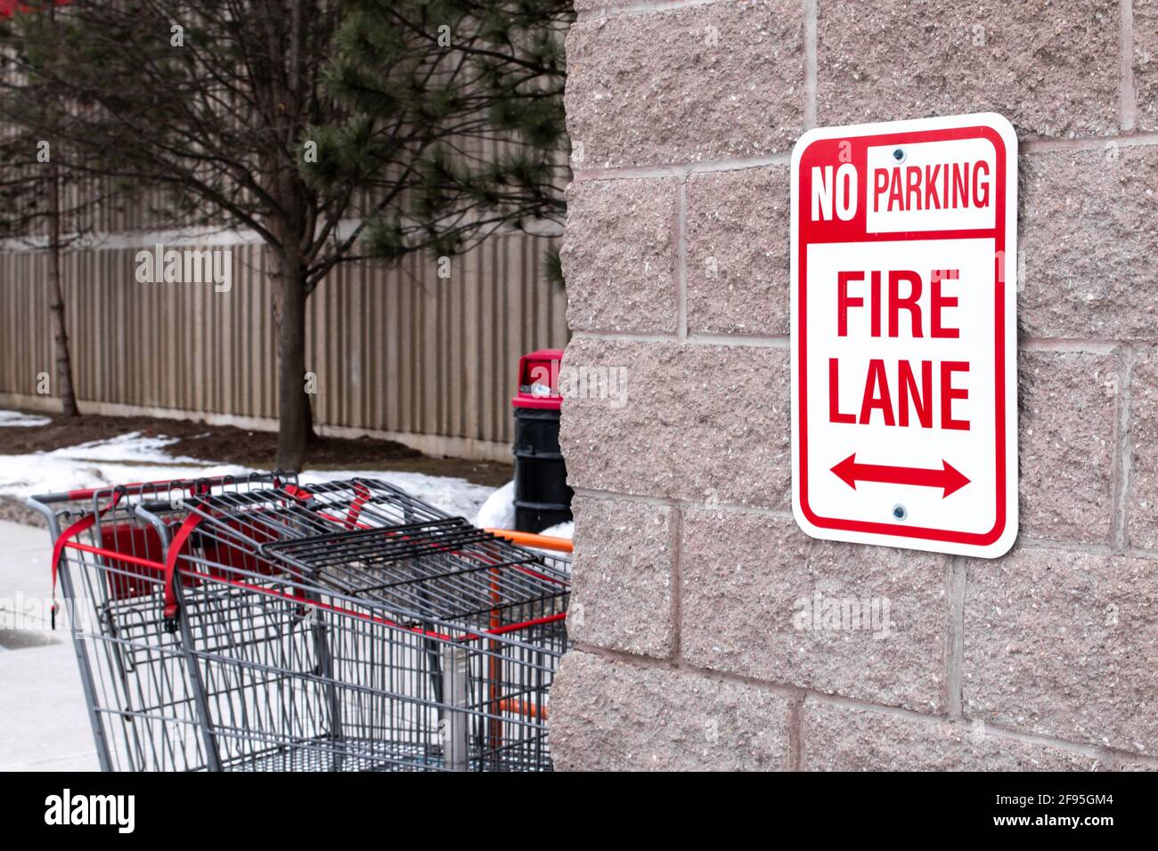 Un panneau vertical rouge « pas de stationnement », Fire Lane avec des flèches à double tête boulonnées à un mur de briques beiges à l'extérieur d'un super marché à London, Ontario, Canada. Banque D'Images