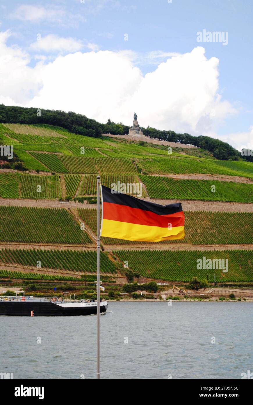 Bingen am Rhein, Allemagne: Rhin avec un bateau, drapeau allemand et vignobles. Niederwalddenkmal, statue de Germania, monument de la réunification allemande. Banque D'Images